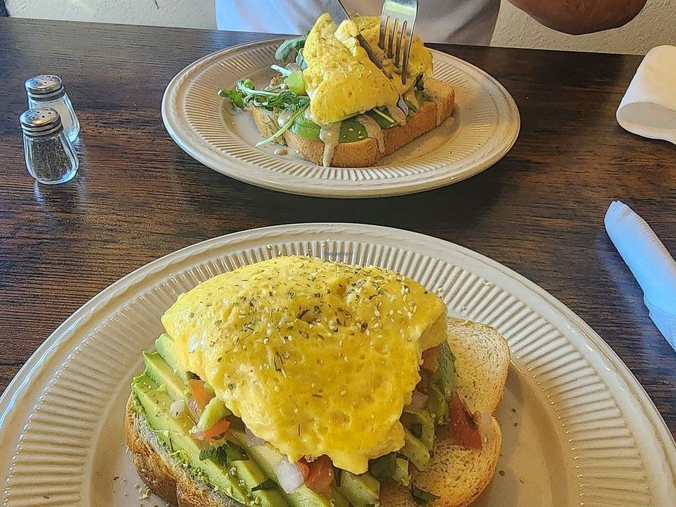 Two brunch plates of omelette on toast, one topped with avocado and tomato.