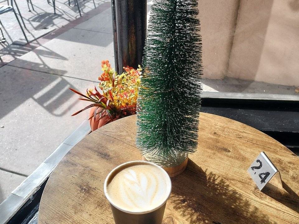 A latte on a wood table by the front window, next to a small bottle-brush tree and a table number.