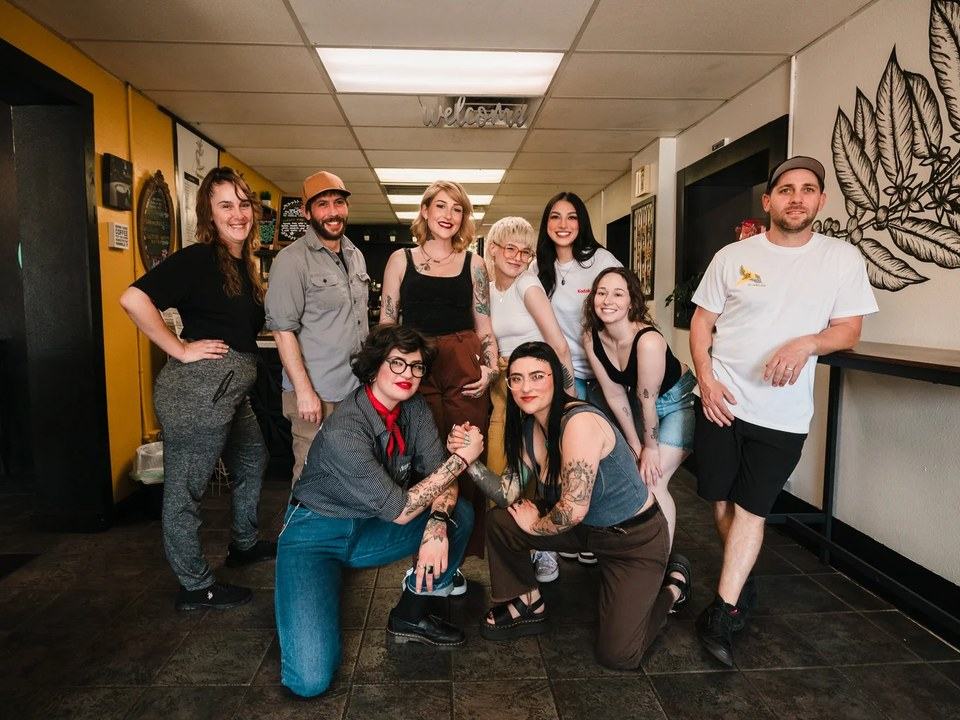 The crew posing inside the shop, in front of a chalkboard and a coffee-plant mural.